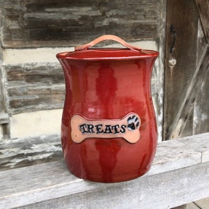 May include: Red ceramic dog treat jar with a bone-shaped lid that says "TREATS" and a paw print.