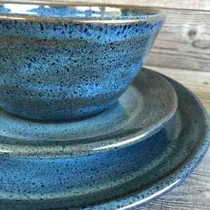 May include: A set of blue ceramic dinnerware with a speckled glaze. The set includes a bowl and two plates.