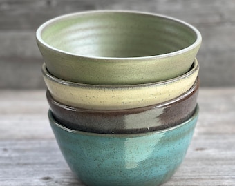 May include: A stack of four ceramic bowls in different colors. The top bowl is green, the second is yellow, the third is brown, and the bottom bowl is teal.