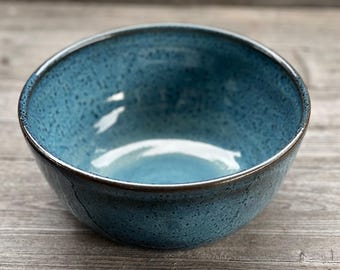 May include: A blue ceramic bowl with a speckled glaze. The bowl is round and has a slight lip.