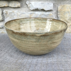 May include: A large, round, ceramic bowl with a speckled, light brown glaze. The bowl has a slightly darker brown rim.