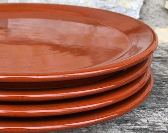 May include: A stack of four terracotta plates, each with a slightly different shade of orange-brown. The plates are smooth and glossy, with a slight sheen.