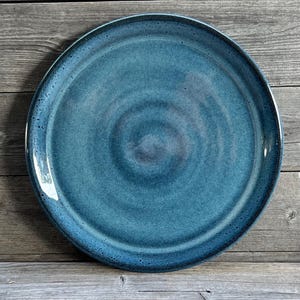 May include: A large, round, blue ceramic plate with a swirling pattern. The plate has a slightly raised rim and a smooth, glossy finish.