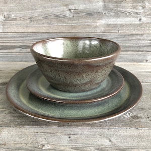 May include: A set of three ceramic dishes in shades of green and brown. The set includes a large plate, a smaller plate, and a bowl.