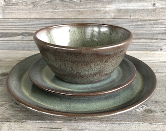 May include: A set of three ceramic dishes in shades of green and brown. The set includes a large plate, a smaller plate, and a bowl.