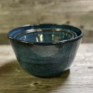 May include: A set of three blue ceramic mixing bowls with a speckled glaze. The bowls are nested inside each other.