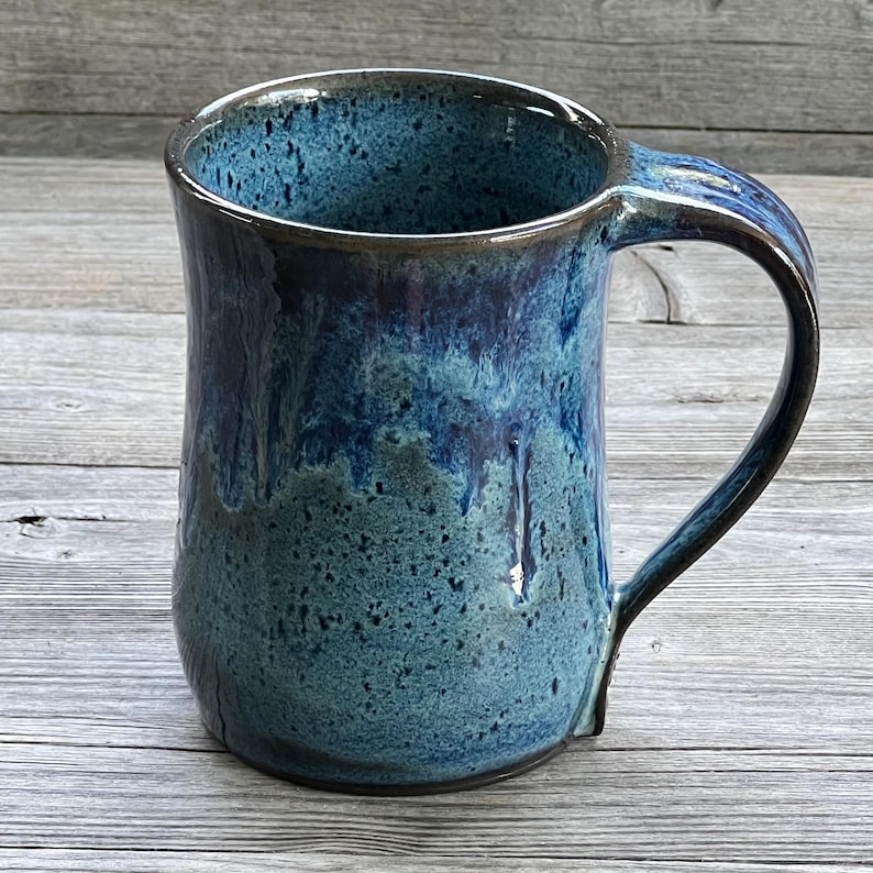 May include: A blue and black ceramic mug with a speckled glaze. The mug has a wide base and a rounded handle.