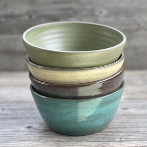 May include: A stack of four ceramic bowls in different colors. The top bowl is green, the second is yellow, the third is brown, and the bottom bowl is teal.