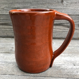 May include: A brown ceramic mug with a rounded body and a handle. The mug has a speckled glaze.