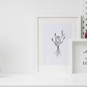 May include: White framed artwork featuring a black line drawing of flowers. A white framed print with the text "all you need is LOVE" sits on a white surface with a vase of pink roses, a white mug, and a small plate with a muffin.