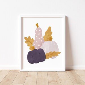 May include: A digital illustration of three gourds in a fall color palette. A pink gourd with white polka dots, a light purple gourd, and a white gourd with a ribbed texture. The gourds are surrounded by gold leaves.