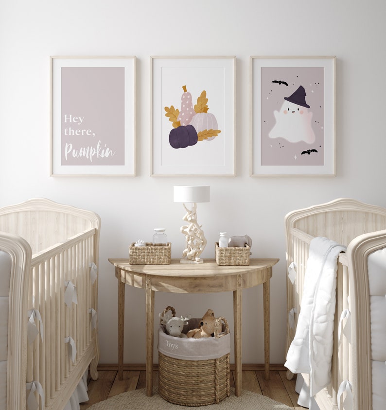 May include: A nursery room with two cribs, a side table with a lamp, and three framed prints on the wall. The prints feature a ghost, pumpkins, and the text "Hey there, Pumpkin".