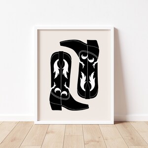 May include: A black and white illustration of two cowboy boots with a white floral design. The boots are on a beige background.