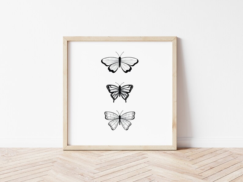 May include: A framed print featuring three black and white butterfly illustrations. Each butterfly has a unique wing pattern, set against a white background. The frame is a light wood color, adding a natural touch to the artwork.