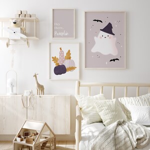 May include: A nursery room with a white wall and a wooden bed with a white blanket and pillows. There are three framed prints on the wall, one with a ghost wearing a witch hat, one with pumpkins and leaves, and one with the text "Hey there, Pumpkin".