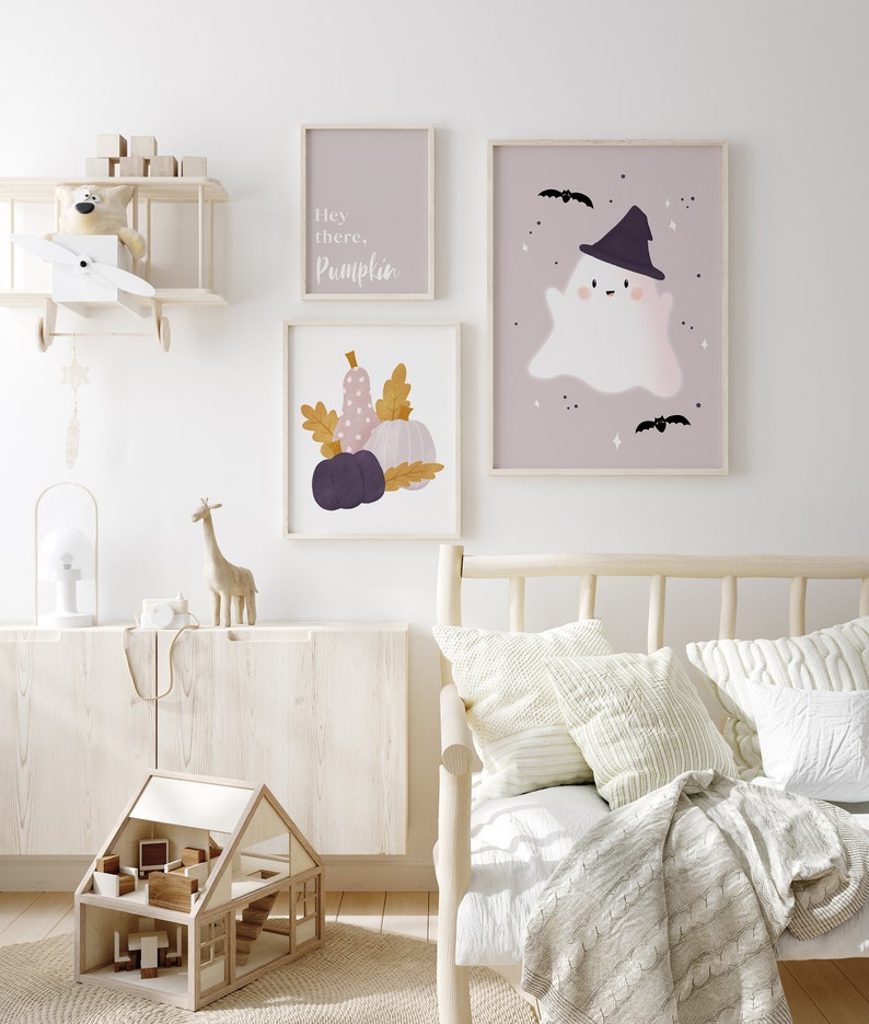May include: A nursery room with a white wall and a wooden bed with a white blanket and pillows. There are three framed prints on the wall, one with a ghost wearing a witch hat, one with pumpkins and leaves, and one with the text "Hey there, Pumpkin".