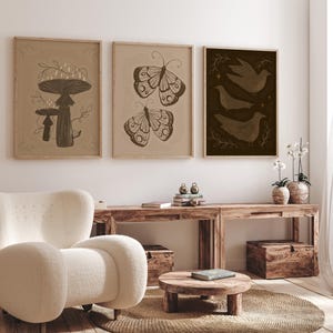 May include: Three framed prints with a minimalist aesthetic. The prints feature a mushroom, a butterfly, and a group of birds. The prints are in a light brown frame and have a beige background.