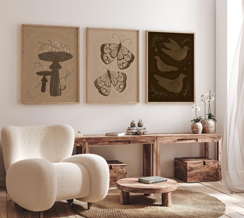 May include: Three framed prints with a minimalist aesthetic. The prints feature a mushroom, a butterfly, and a group of birds. The prints are in a light brown frame and have a beige background.