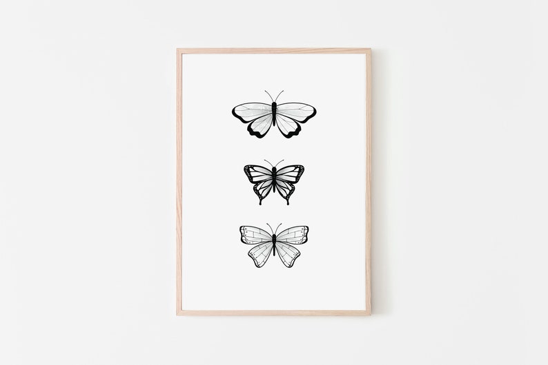 May include: A framed print featuring three stylized butterfly illustrations in black and white. Each butterfly has a unique wing pattern, with the artwork set against a white background. The frame is a light wood color.