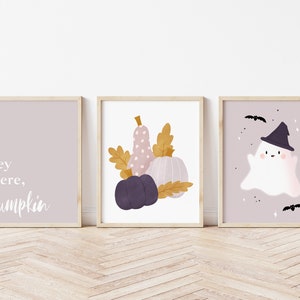 May include: Three printable Halloween themed wall art prints. The first print has a light purple background with the text "Hey there, Pumpkin". The second print has a light purple background with a pink and white pumpkin, a purple pumpkin, and a brown leaf. The third print has a light purple background with a white ghost wearing a black witch hat and a black bat flying above.