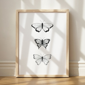 May include: A framed print featuring three black and white butterfly illustrations. Each butterfly has a unique wing pattern, set against a white background. The frame is made of light-colored wood, adding a natural touch to the artwork.
