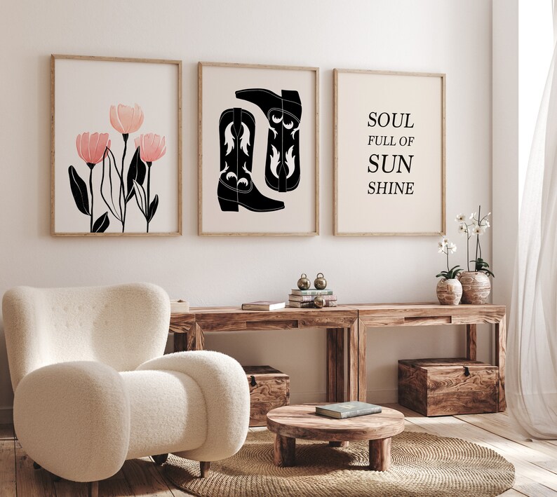May include: Three framed prints on a white wall. The left print features a black and white illustration of pink flowers. The middle print features a black and white illustration of two cowboy boots. The right print features the text "SOUL FULL OF SUNSHINE".
