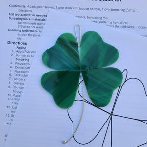 May include: A stained glass kit for a four-leaf clover. The kit includes four dark green glass leaves, a wire stem, and a pattern. The clover is a vibrant green with a textured appearance, perfect for a DIY stained glass project.