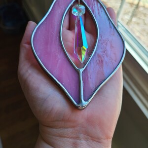 Puede incluir: Un atrapasol de vidrio tintado de color rosa con un prisma de cristal iridiscente transparente colgando en el centro.