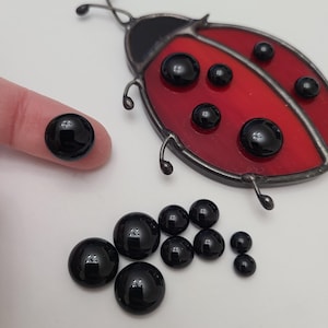 May include: A red and black stained glass ladybug with black glass beads. Several loose black glass beads of varying sizes are also present. Text on the image reads: Completed project for size comparison and inspiration purposes only. Project not included in purchase.