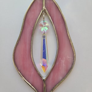 Puede incluir: Un atrapasol de vidrio tintado de color rosa con un prisma de cristal colgando de &eacute;l. El atrapasol tiene la forma de una hoja estilizada con una abertura en forma de l&aacute;grima en el centro.