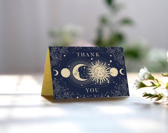 May include: A navy blue thank you card with a gold border. The card features a celestial design with a sun and moon in the center. The text "THANK YOU" is printed in gold lettering.