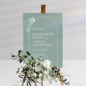 May include: A light blue wedding announcement sign with a white arch and floral design. The text reads "Welcome to the wedding of Josephine Strik and Adric Vikuckis 20.12.2024 Urban Brisbane 345 Wickham Tce Brisbane 4000".