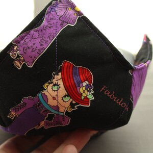 Puede incluir: Tazón de tela negro con un diseño de dibujos animados morado y rojo. El tazón tiene una costura blanca y la palabra "Fabulous" está impresa en el lateral.