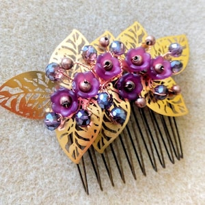 Op de afbeelding: Gouden haar kam met drie bladeren versierd met paarse bloemen en iriserende kralen.