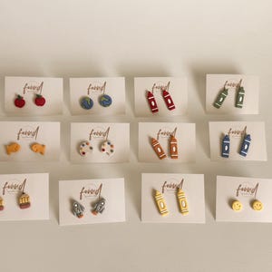 May include: A collection of stud earrings on white cards. The earrings feature various designs, including apples, globes, crayons, fish, paint palettes, pencils, rockets, and smiley faces. Each card has the word "found" printed on it.