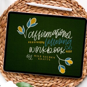 May include: A digital illustration of a green background with white text that reads "Affirmations Lettering Workbook by Wild Salmon Crafts". The text is surrounded by yellow and blue floral designs.