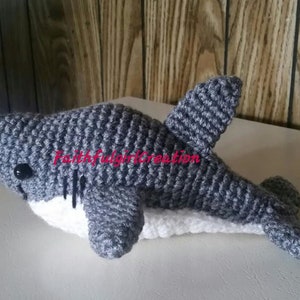 May include: A gray crocheted shark plush toy with white crocheted belly and black eyes.