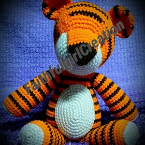 May include: A crocheted tiger stuffed animal with orange and black stripes. The tiger has a light blue belly and a black nose. The text "Faithfulgirlcreation" is visible on the tiger's side.