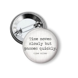 May include: A round button pin with a silver metal backing and a white face. The face features the quote "Time moves slowly but passes quickly." by Alice Walker in black text. The pin is a classic accessory.
