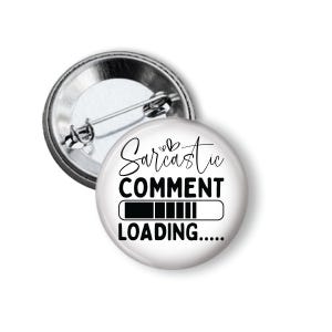 May include: A white button with the text "Sarcastic Comment Loading....." in black script and block letters. The button has a silver metal backing and a pin. The design includes a loading bar graphic.
