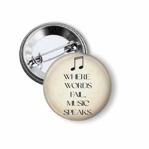 May include: A round button with a musical note and the text "WHERE WORDS FAIL, MUSIC SPEAKS." The button has a cream-colored background and a silver metal pin backing. The text and musical note are black.