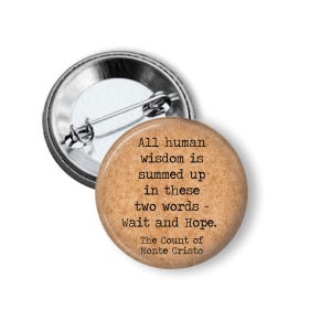 May include: A round button pin with a quote from "The Count of Monte Cristo." The pin has a tan background with black text that reads "All human wisdom is summed up in these two words - Wait and Hope."