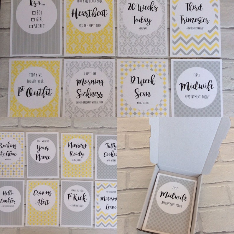 Pu&ograve; includere: Un set di biglietti di pietre miliari della gravidanza in una scatola bianca. Le carte presentano testo nero e giallo su sfondo grigio. Le frasi includono "Heartbeat", "20 Weeks Today" e "First Midwife Appointment Today."