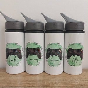 May include: Four white water bottles with black lids and grey spouts. Each bottle has a green and white design with a video game controller and the text "Sleep Game Repeat Eat Sleep Game" and a name: Harley, Tommy, Roman, and Alfie.