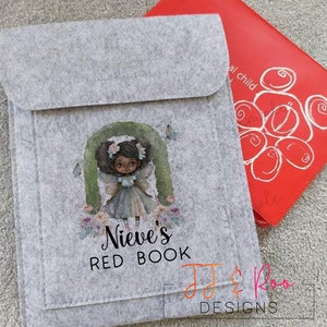 May include: A gray felt book cover with a colorful illustration of a fairy with brown skin and wings. The text "Nieve's Red Book" is printed below the illustration. The text "JJ & Roo Designs" is printed in the bottom right corner.
