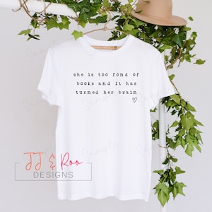 May include: White t-shirt with black text that reads "she is too fond of books and it has turned her brain" with a small heart symbol.