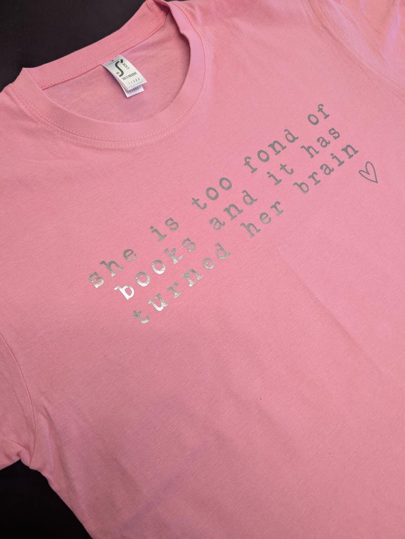 May include: Pink t-shirt with a silver glitter design that says "She is too fond of books and it has turned her brain &hearts;".