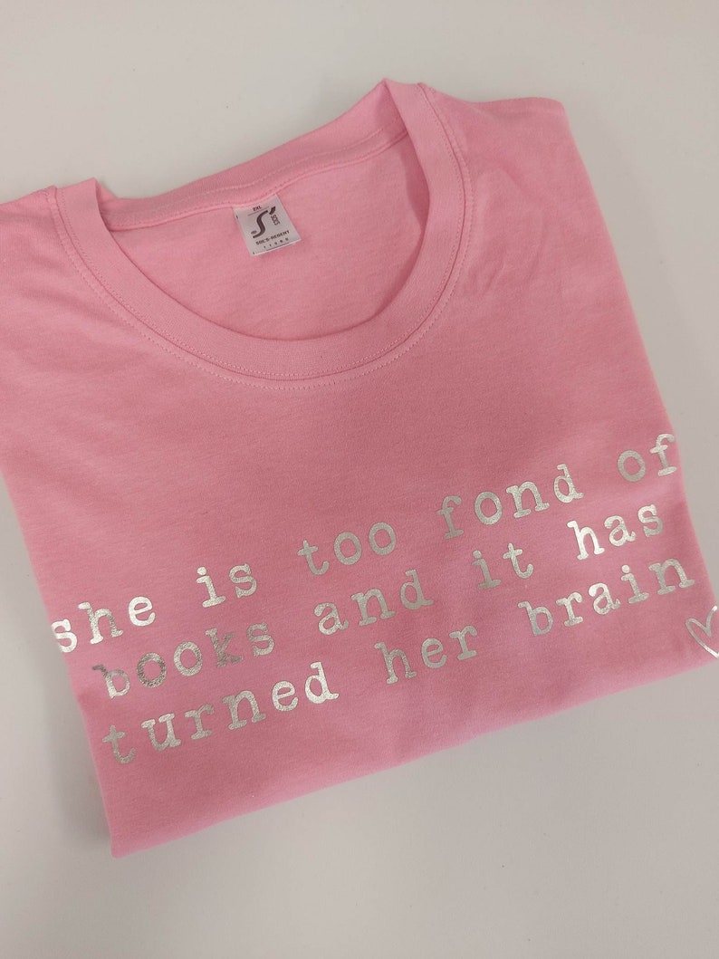May include: Pink t-shirt with silver lettering that reads "She is too fond of books and it has turned her brain"