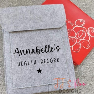 May include: A gray felt folder with a pocket on the front. The folder has the text "Annabelle's Health Record" and a star printed on the front. The folder is sitting on top of a red folder with a white design.