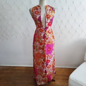 May include: A long, sleeveless maxi dress with a floral print in shades of pink, orange, and brown. The dress has a button-up front and a plunging neckline.